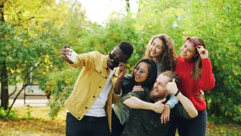 Group of diverse friends laughing and taking a selfie in a park, representing life skills therapy conversations friendships dating and the joy of building authentic social connections