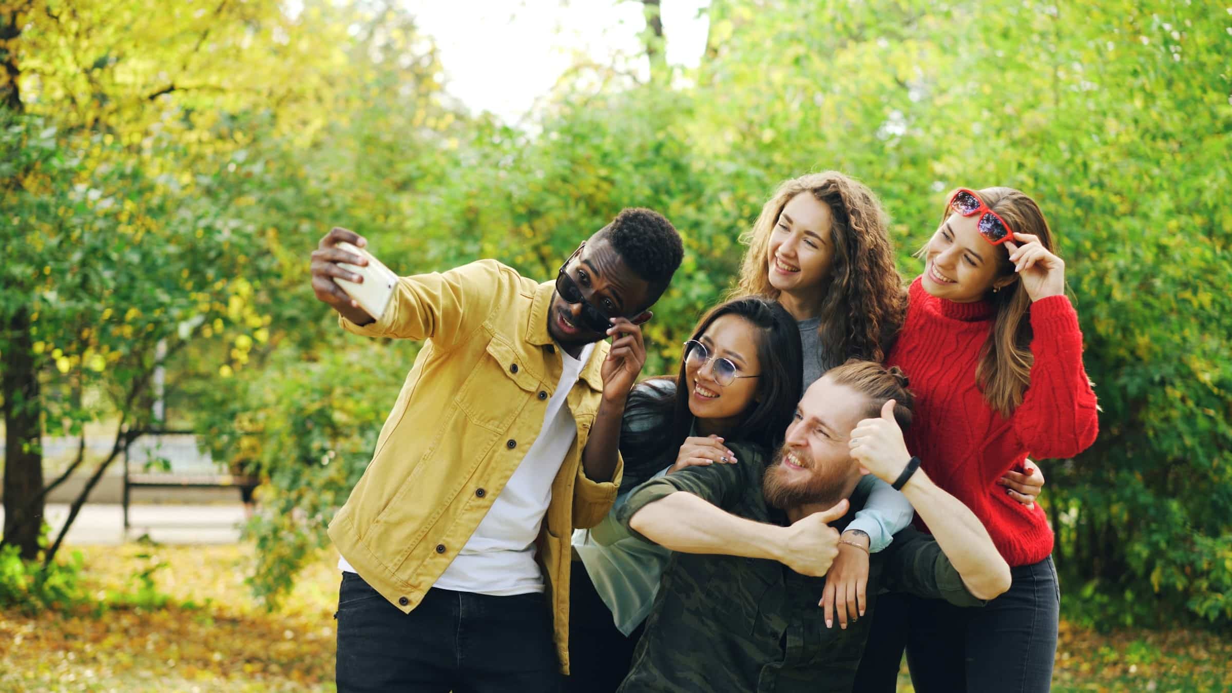 Group of diverse friends laughing and taking a selfie outdoors in a park, symbolizing connection, confidence, and joy in social relationships