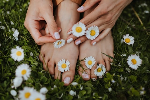 Hands placing daisies on feet in grass, representing sensory grounding used in occupational therapy