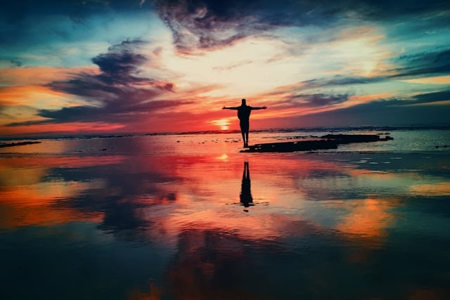 Person standing with open arms at sunset, symbolizing balance, mindfulness, and emotional wellbeing in occupational therapy