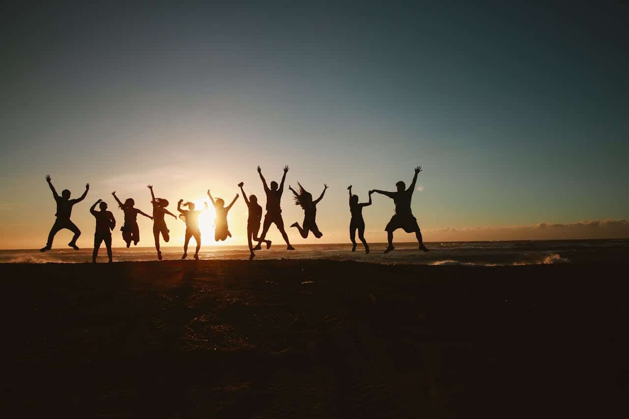A group of people jumping together at the beach during sunset, symbolizing community support and shared healing.