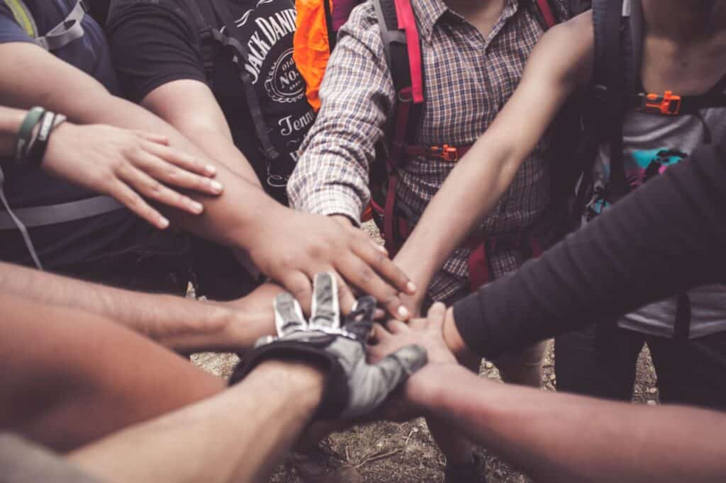 A close-up of multiple hands stacked together in a team huddle, representing peer support and unity in community therapy.