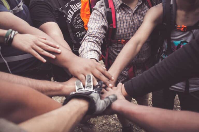A close-up of multiple hands stacked together in a team huddle, representing peer support and unity in community therapy.