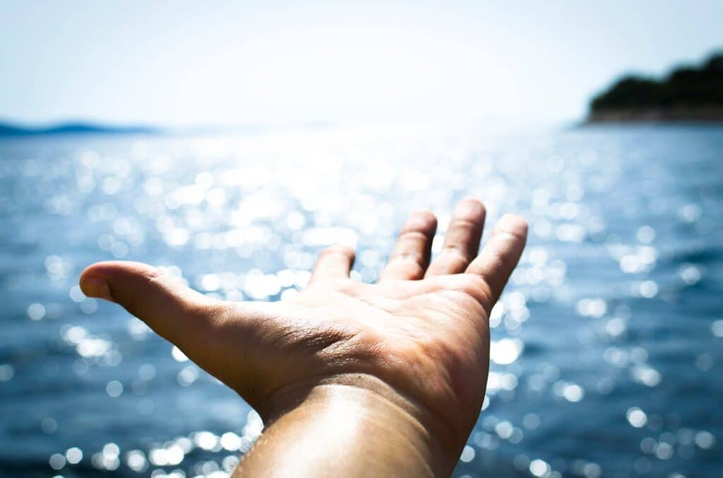 outstretched hand reaching toward bright ocean water, symbolizing hope and emotional release