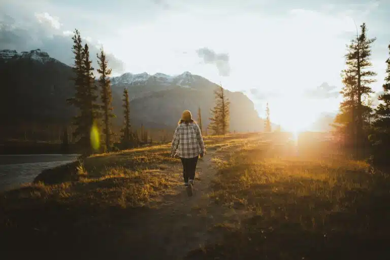 A person walking a wooded path toward sunlight, symbolizing therapy for life changes, healing, and new beginnings.