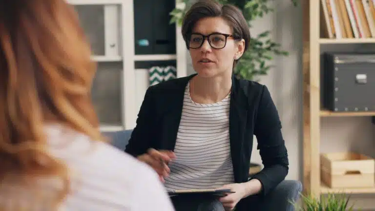 OT vs talk therapy for anxiety illustrated by a therapist meeting one‑on‑one with an adult client in a calm office setting