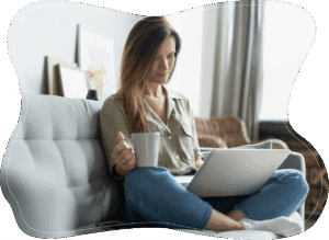 Woman holding a cup of coffee while using a laptop, engaged posture suggesting learning and curiosity