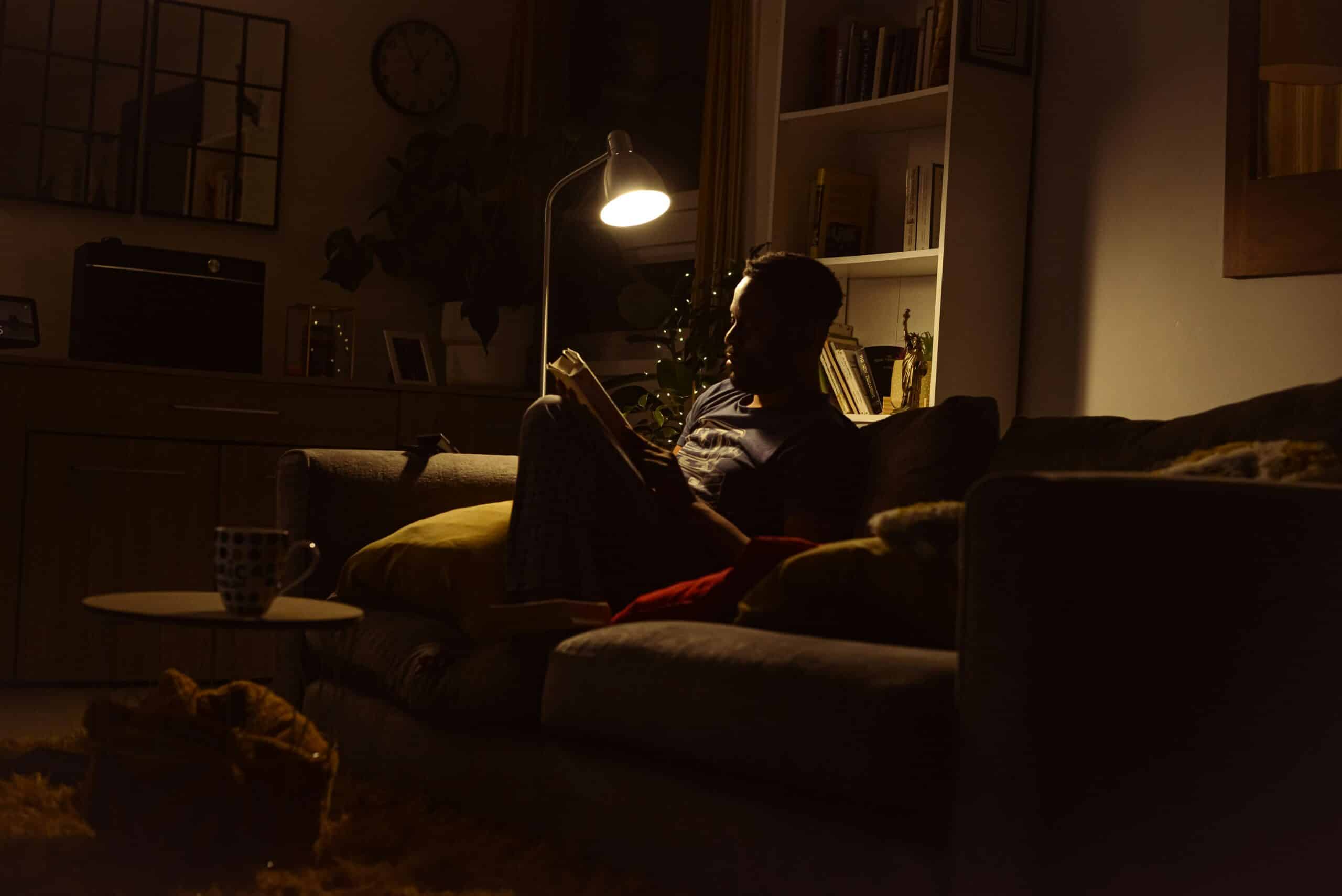 Adult sitting on a couch in a dimly lit living room, reading under a single warm lamp, with a calm and quiet environment suggesting recovery after a long, overstimulating day.