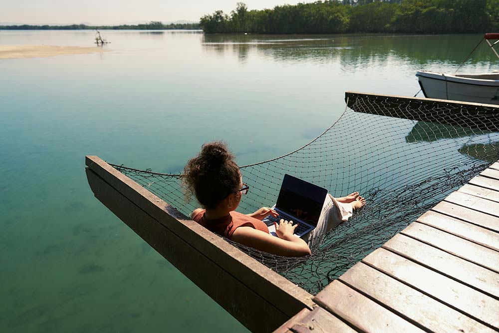 A woman sitting on a dock using a laptop computer
