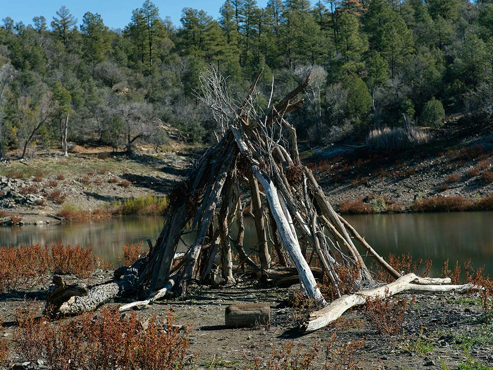 Rustic teepee made of branches near a body of water
