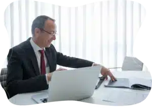 A businessman smiling while working at a white desk with a laptop.