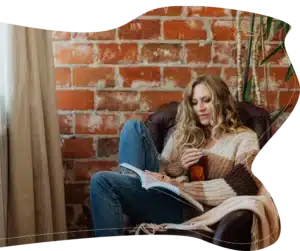A peaceful portrait of a woman enjoying a mindful afternoon reading a book and sipping hot tea in a cozy, rustic living room setup.