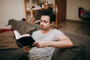 A man enjoying a quiet, cozy afternoon reading a book while lounging comfortably on his living room couch.