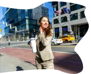 A smiling woman in a beige suit holding a white travel mug on a city street.