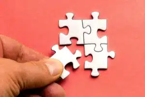 A hand placing a white puzzle piece to complete a jigsaw puzzle on a red background.