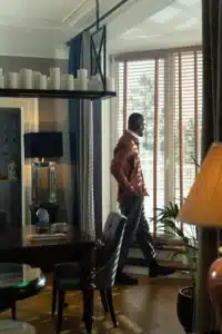 A man standing by a window with wooden blinds in a dining room.