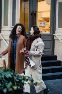 Two women walking down a city street with shopping bags while laughing together.